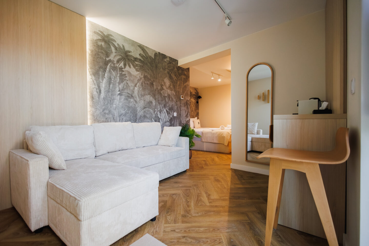 Living premium cu tapet tropical, canapea albă și bucătărie deschisă.