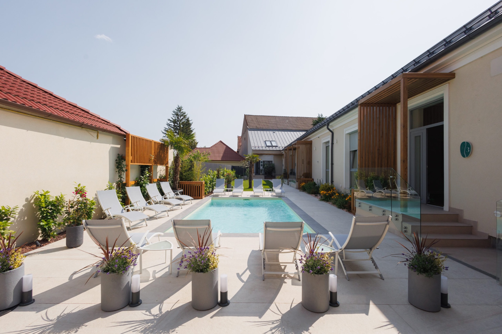Piscina exterioară cu șezlonguri albe și pergolă de lemn.
